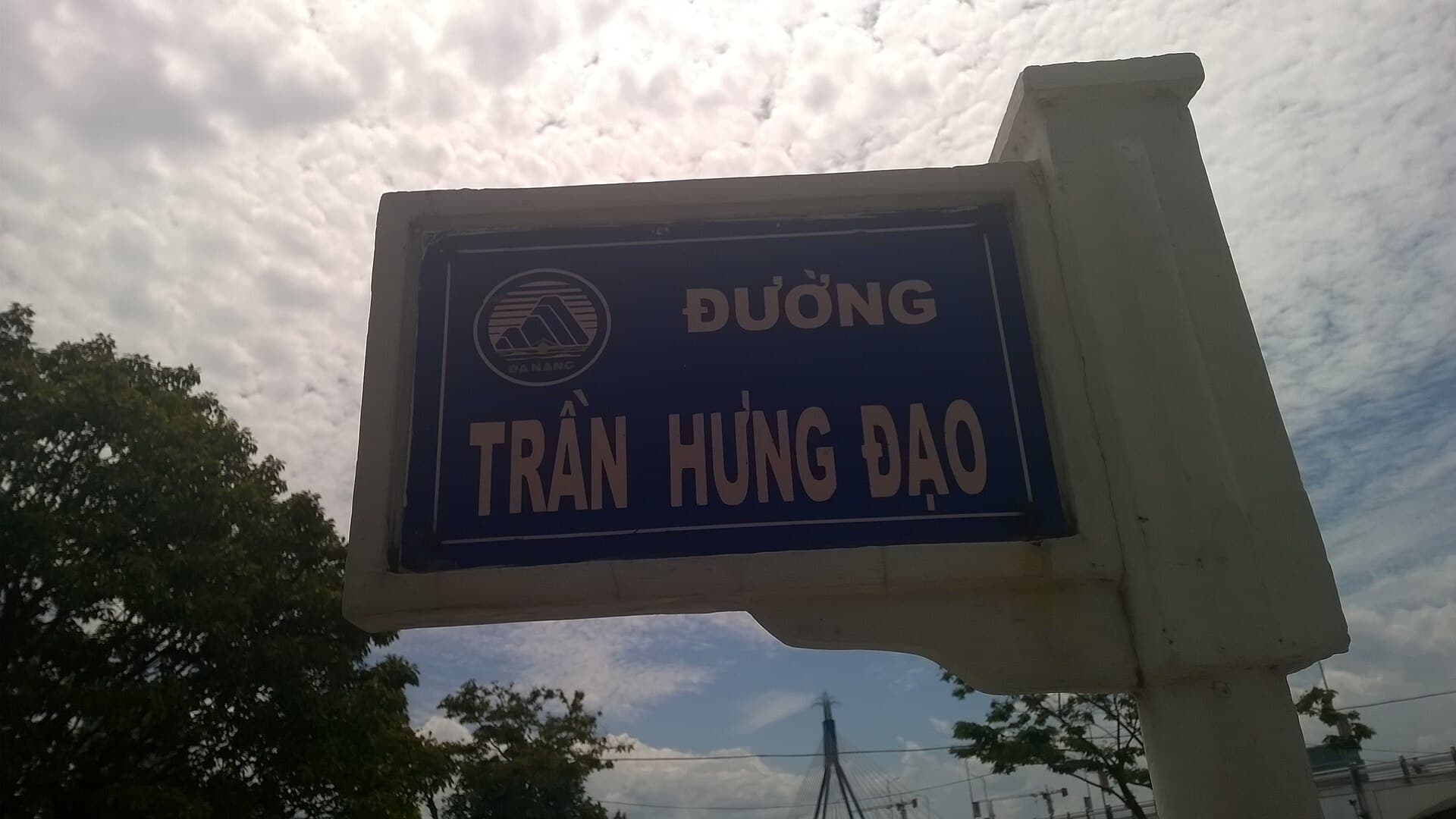 Уличная табличка «Đường Trần Hưng Đạo» с гербом Дананга на бетонном столбе