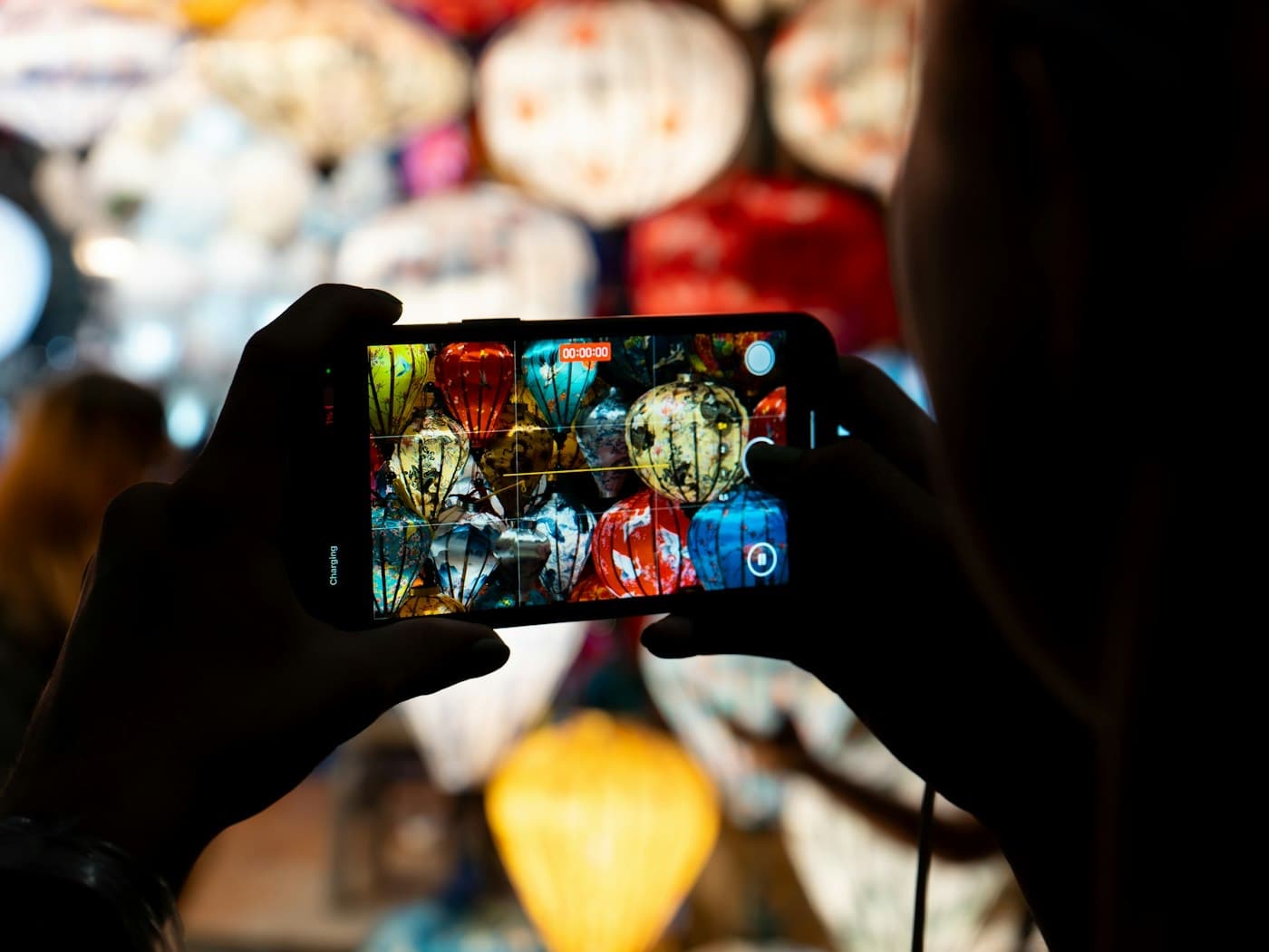 Tourist filming silk lanterns in a Hoi An shop on a smartphone in the evening