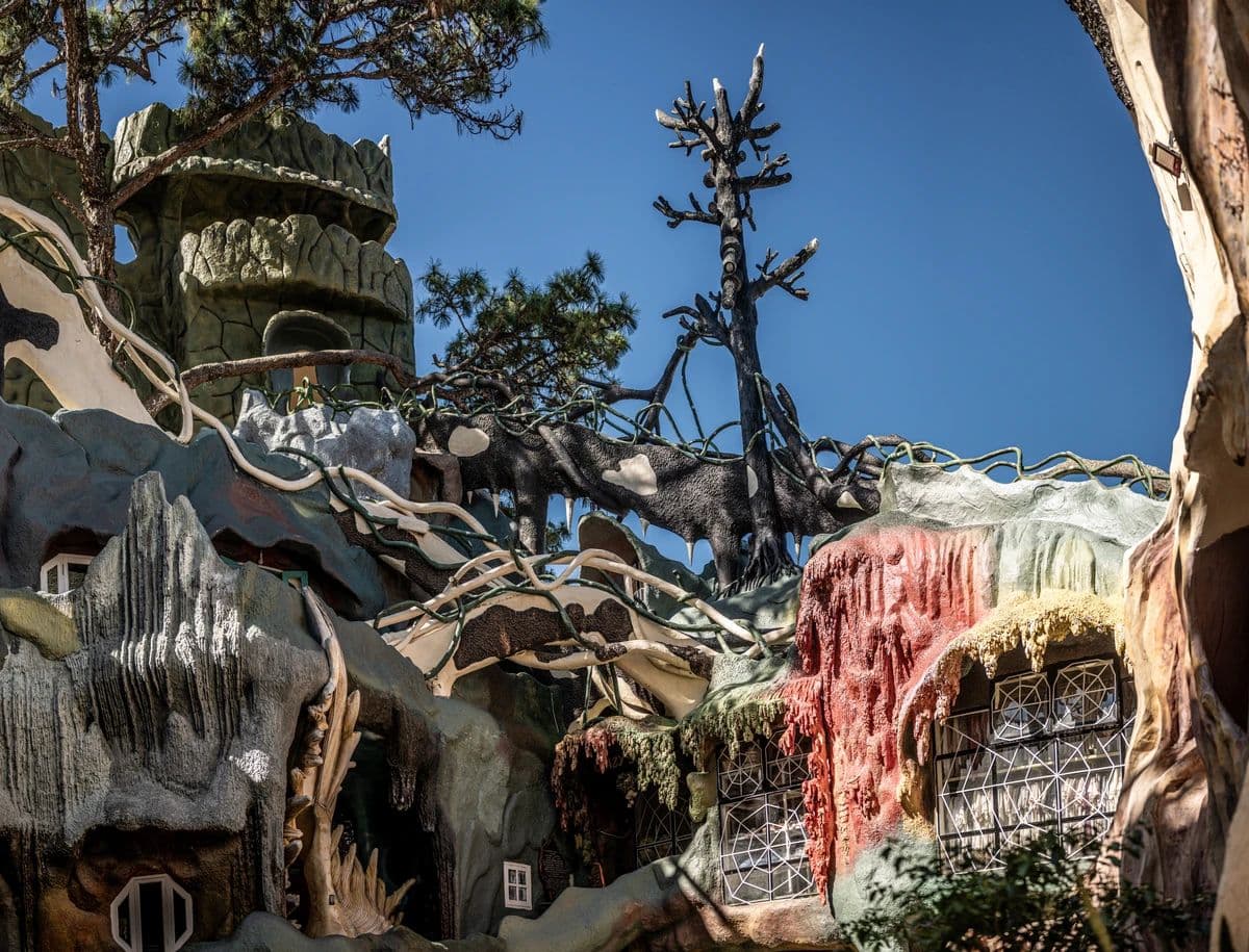 Причудливые стены Crazy House в Далате: наплывы, корни и сухое дерево на фоне неба