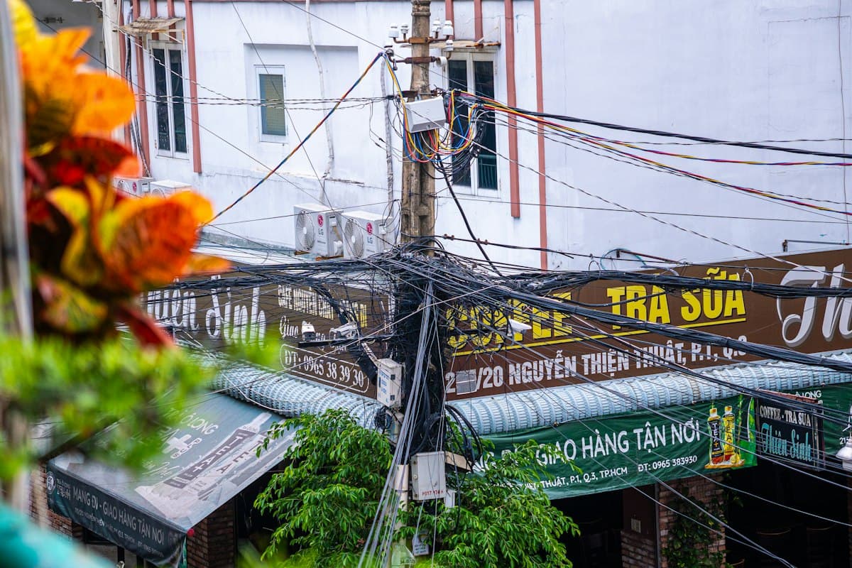 Tangled overhead power lines above a Vietnamese street lined with cafe signs