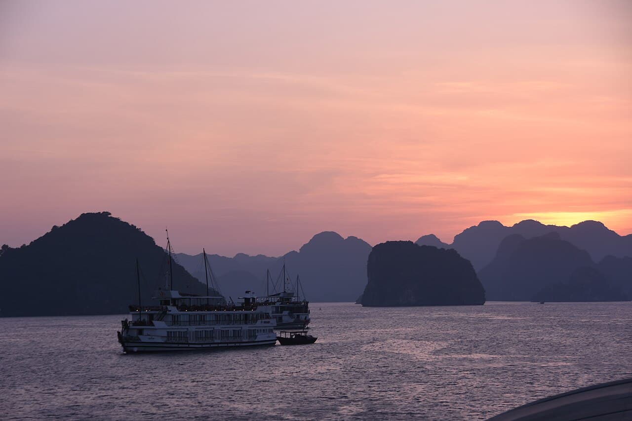 Limestone karsts of Halong Bay at sunset with a cruise junk
