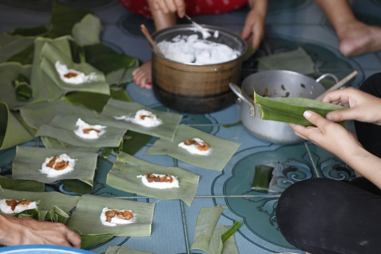 Руки раскладывают рисовое тесто с креветкой на банановые листья на кулинарном занятии