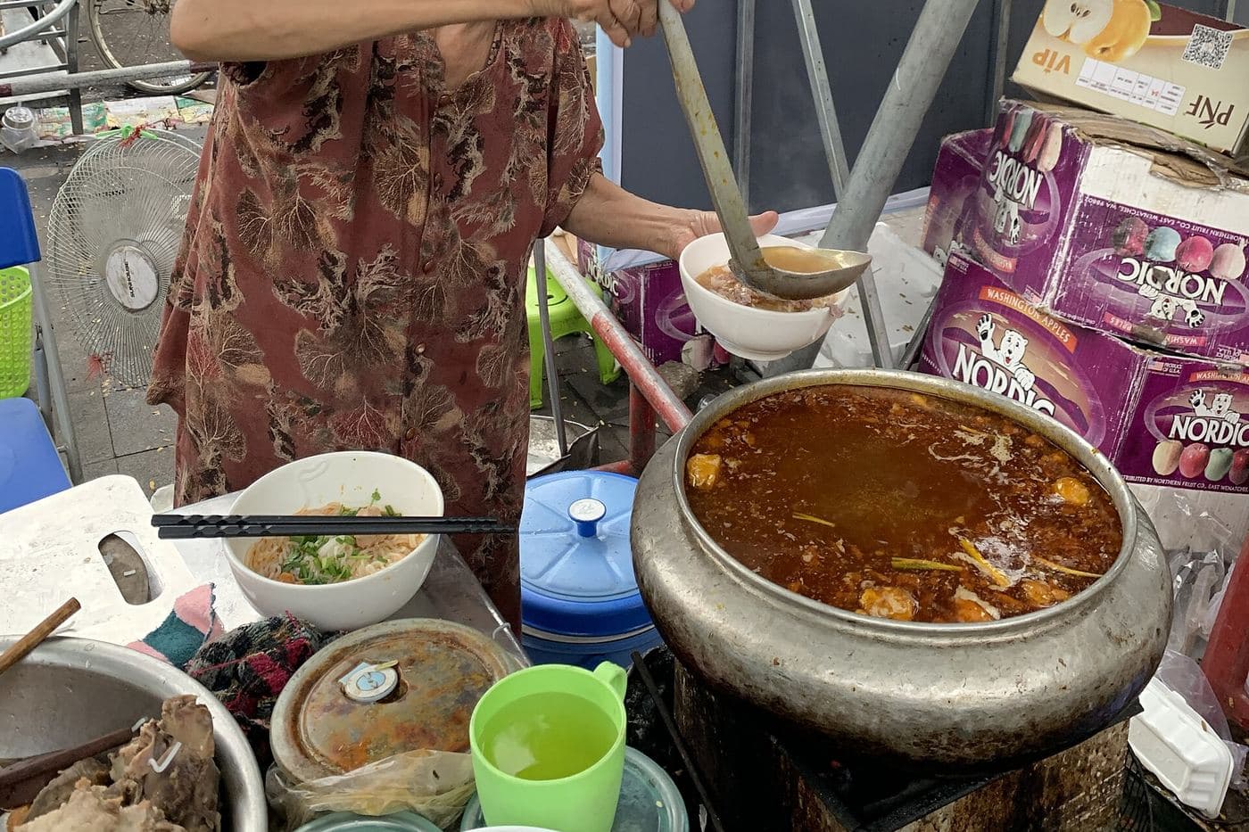 Уличная торговка разливает bún bò Huế из большого котла у рынка Донгба