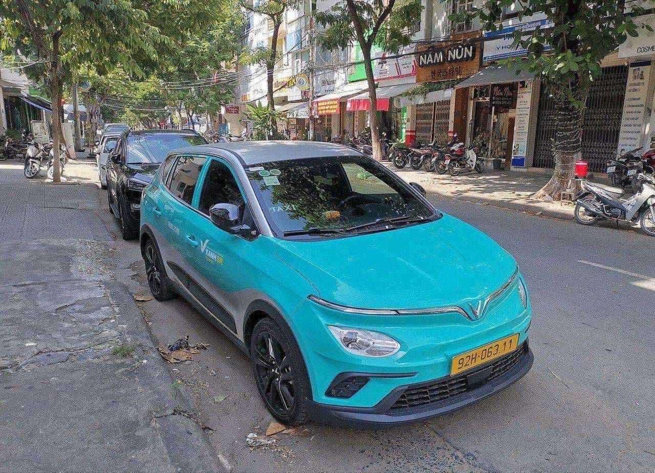 Бирюзовый электромобиль VinFast VF e34 службы Xanh SM у тротуара вьетнамской улицы