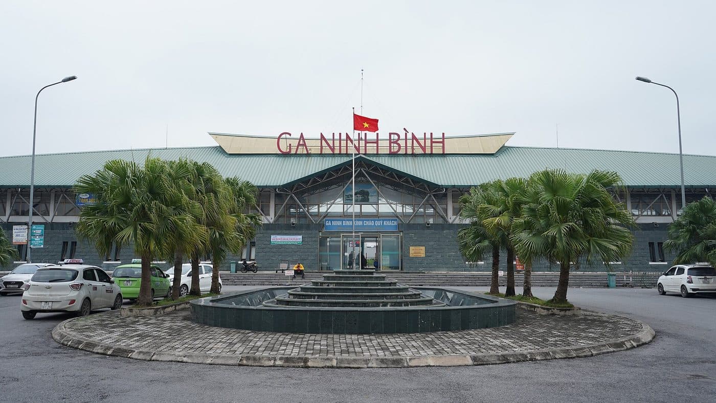 Здание вокзала Ниньбиня с вывеской Ga Ninh Bình, пальмы и такси на привокзальной площади