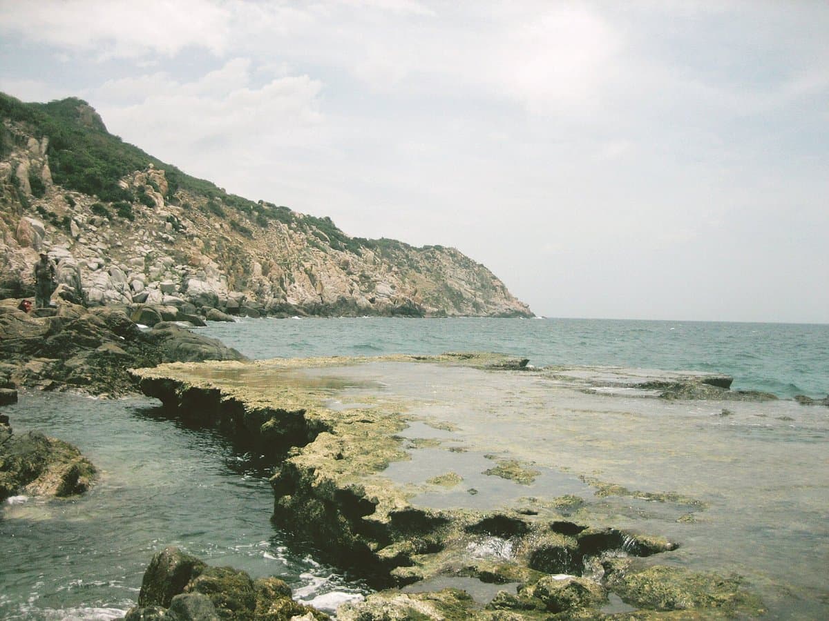 Flat coral shelves of Hang Rai at the water's edge below a rocky headland