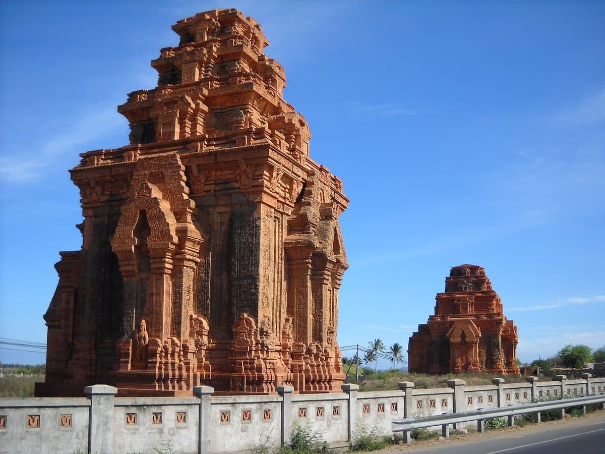 Two brick towers of Hoa Lai behind a fence by Highway QL1