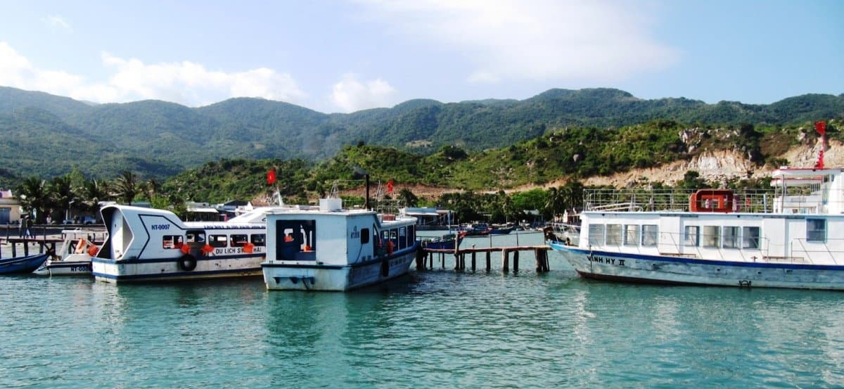 Tour boats moored at the Vinh Hy Bay pier below the hills