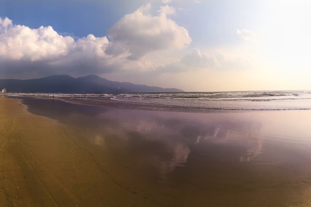 Широкий вьетнамский пляж с мокрым песком и горами на горизонте