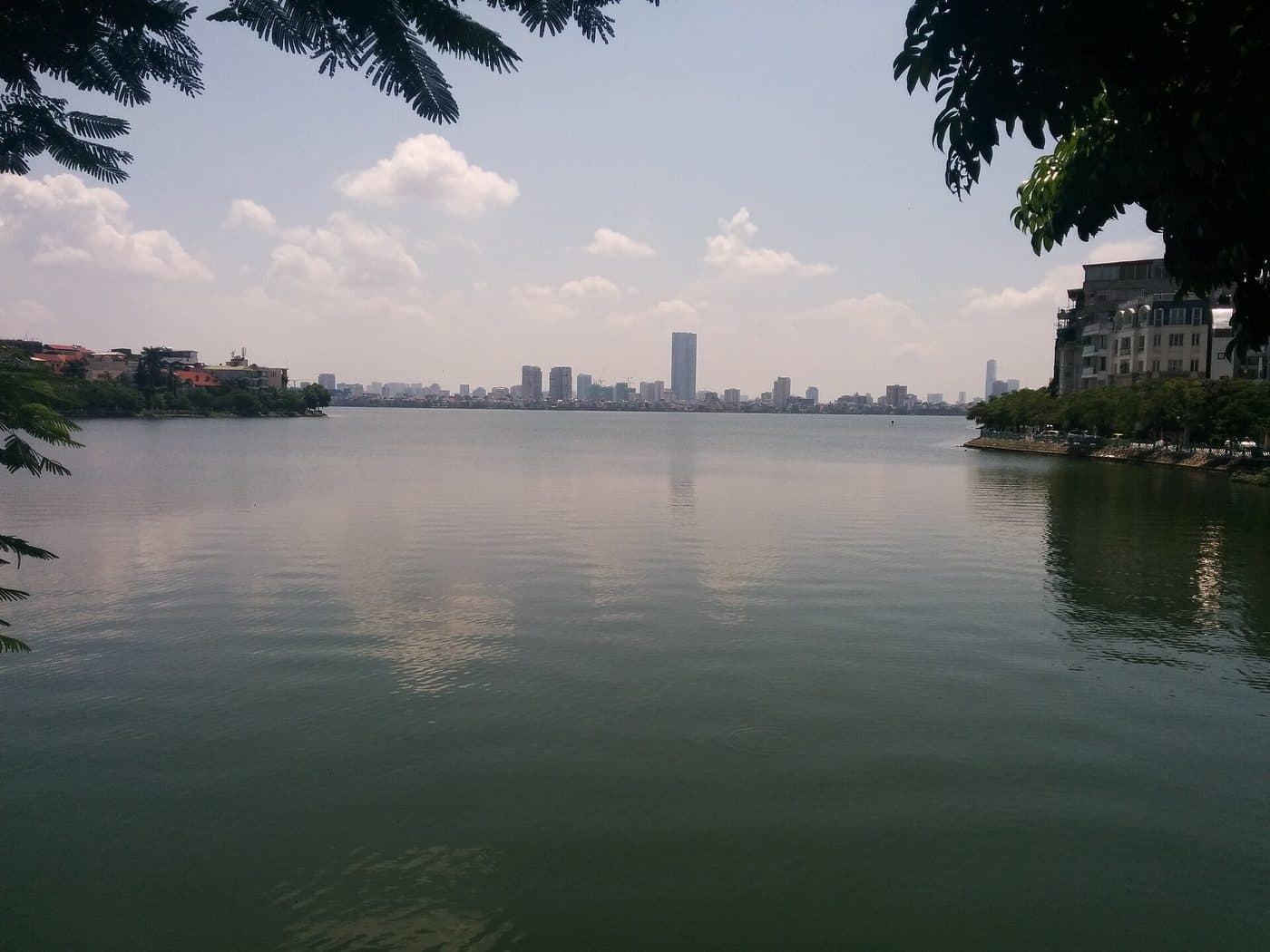 West Lake in Hanoi on a sunny day: calm water, lakeside houses and city towers in the distance