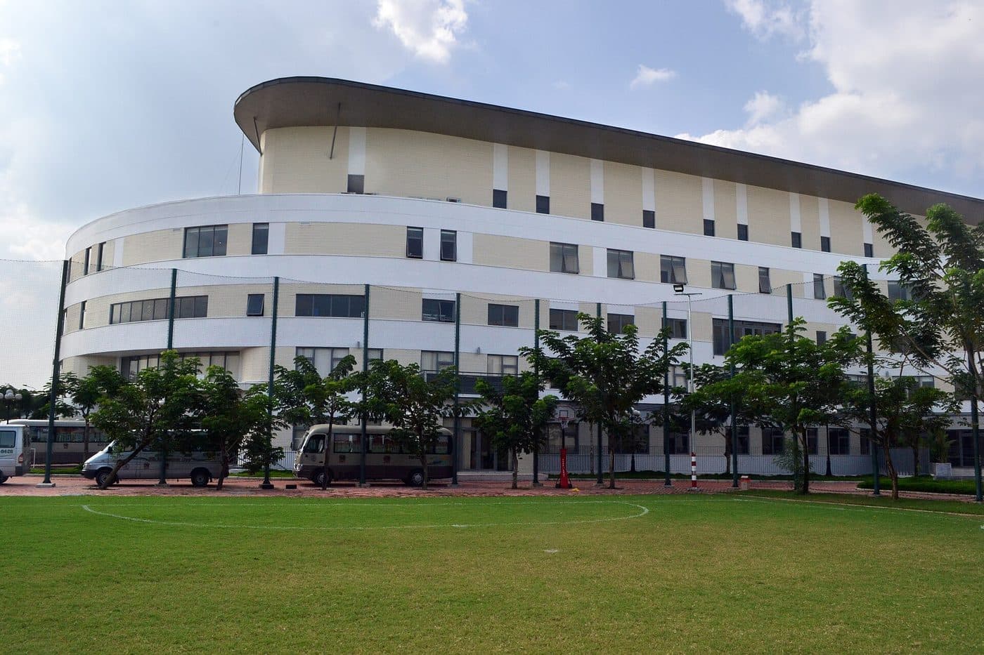 School minibuses parked by the BVIS international school building in Ho Chi Minh City, with a football field in front
