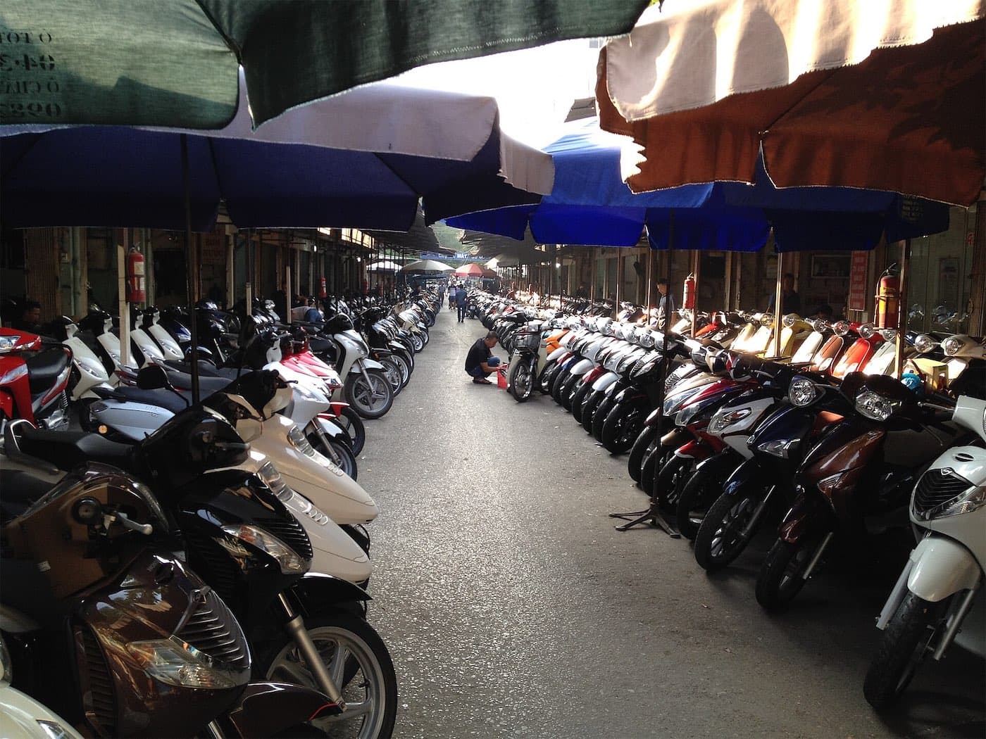 Rows of scooters under umbrellas at a used motorbike market in Hanoi