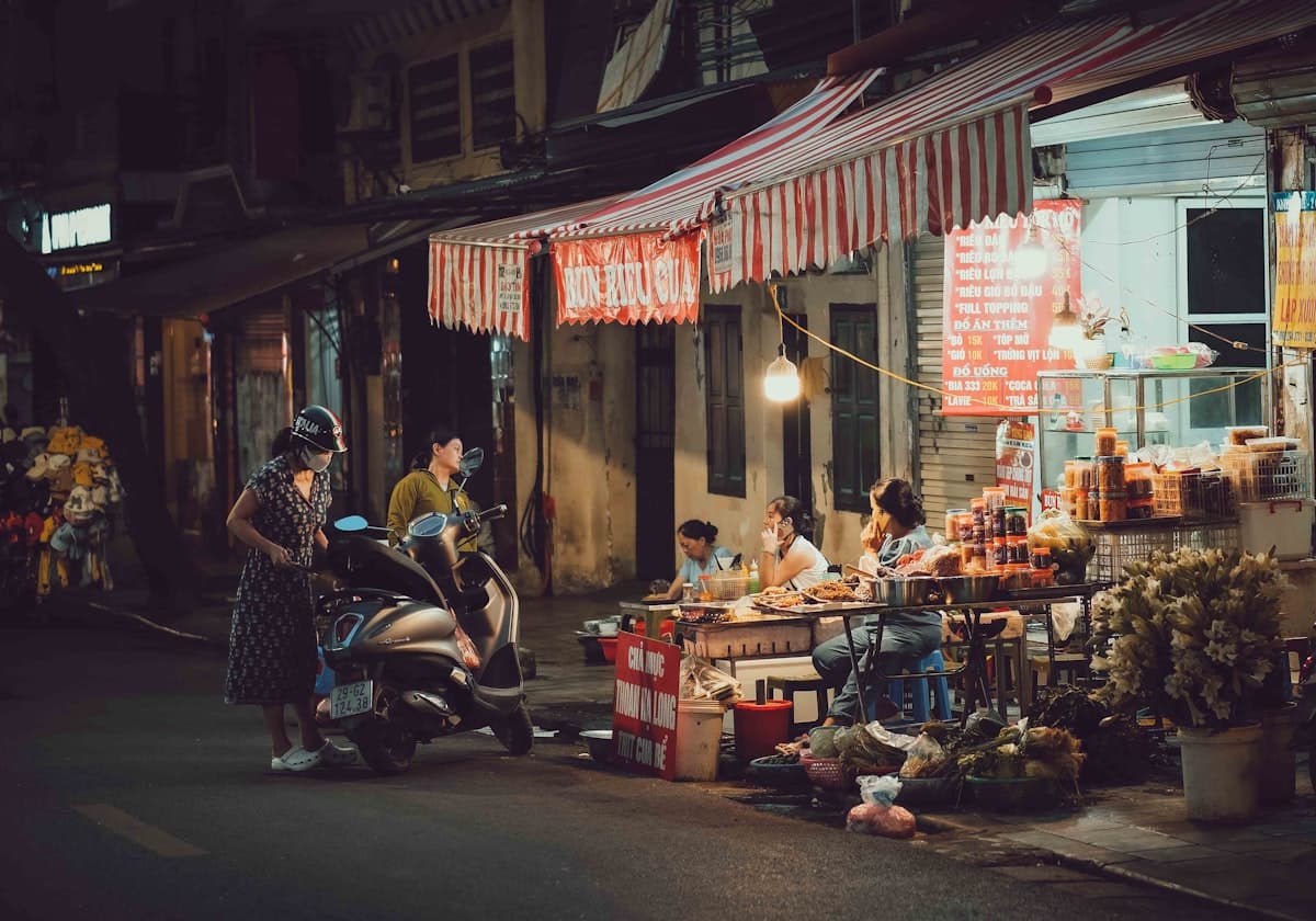 Вьетнамская уличная фошница ночью с навесом, продавщицей и местными жителями у мотоциклов