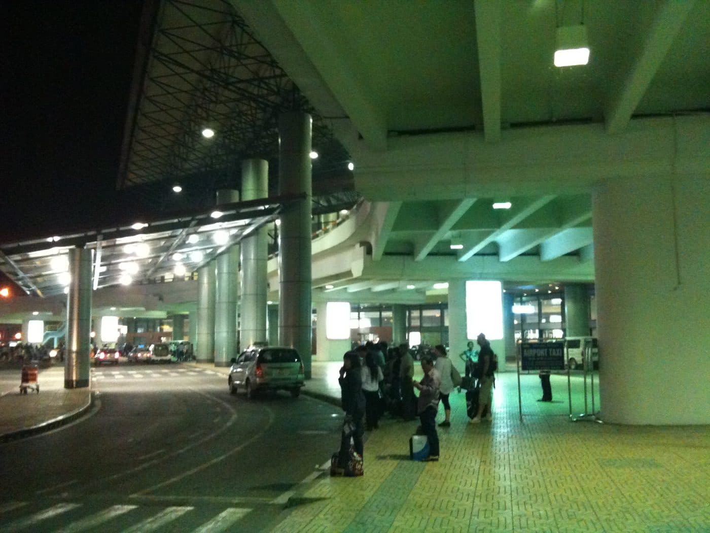 Зона прилёта аэропорта Нойбай ночью, табличка Airport Taxi и пассажиры с багажом