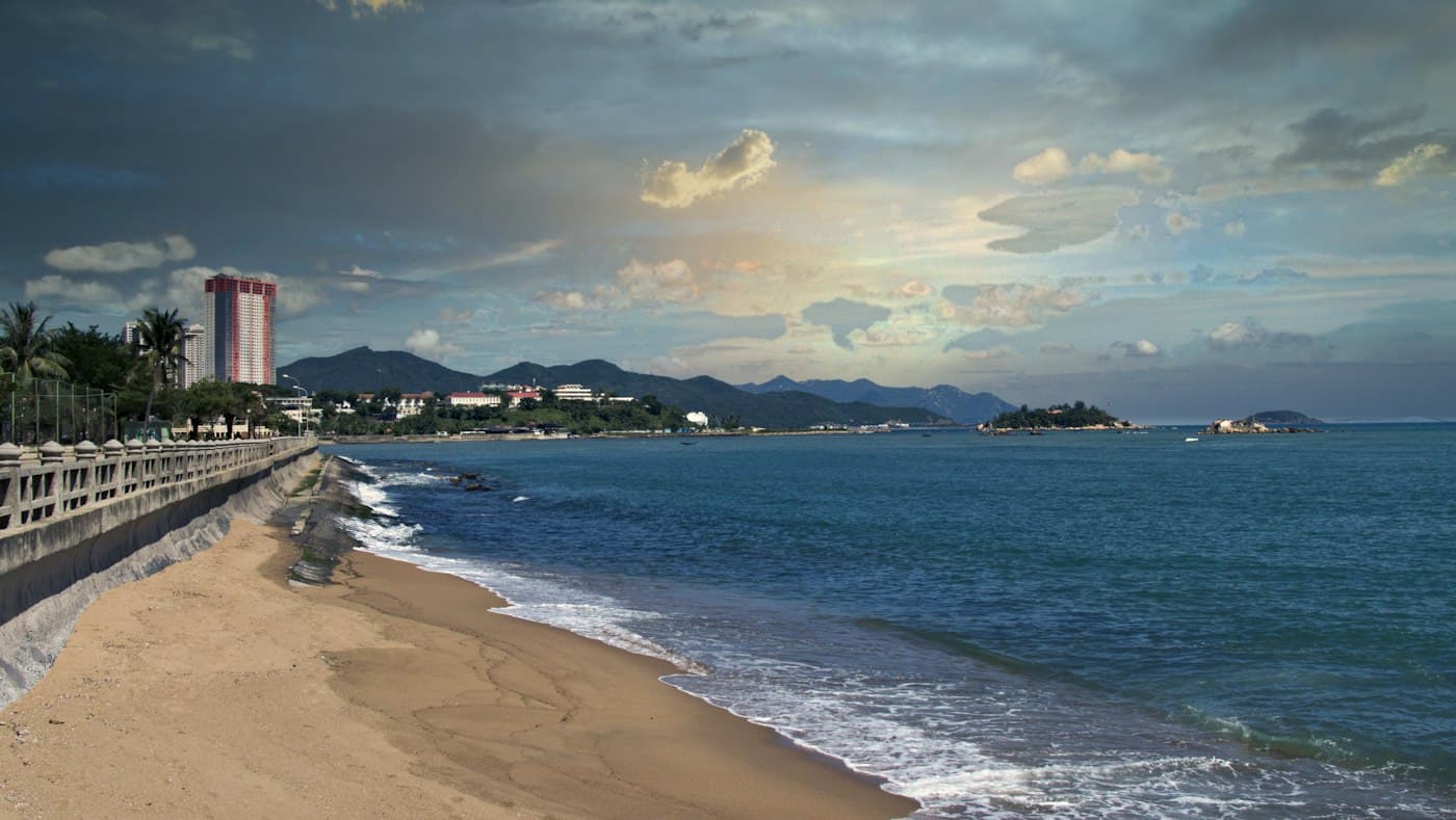 Nha Trang seafront promenade with a sandy beach and surf under a cloudy sky