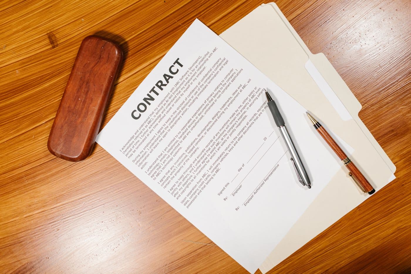 An employment contract form with employer signature fields and two pens on a desk