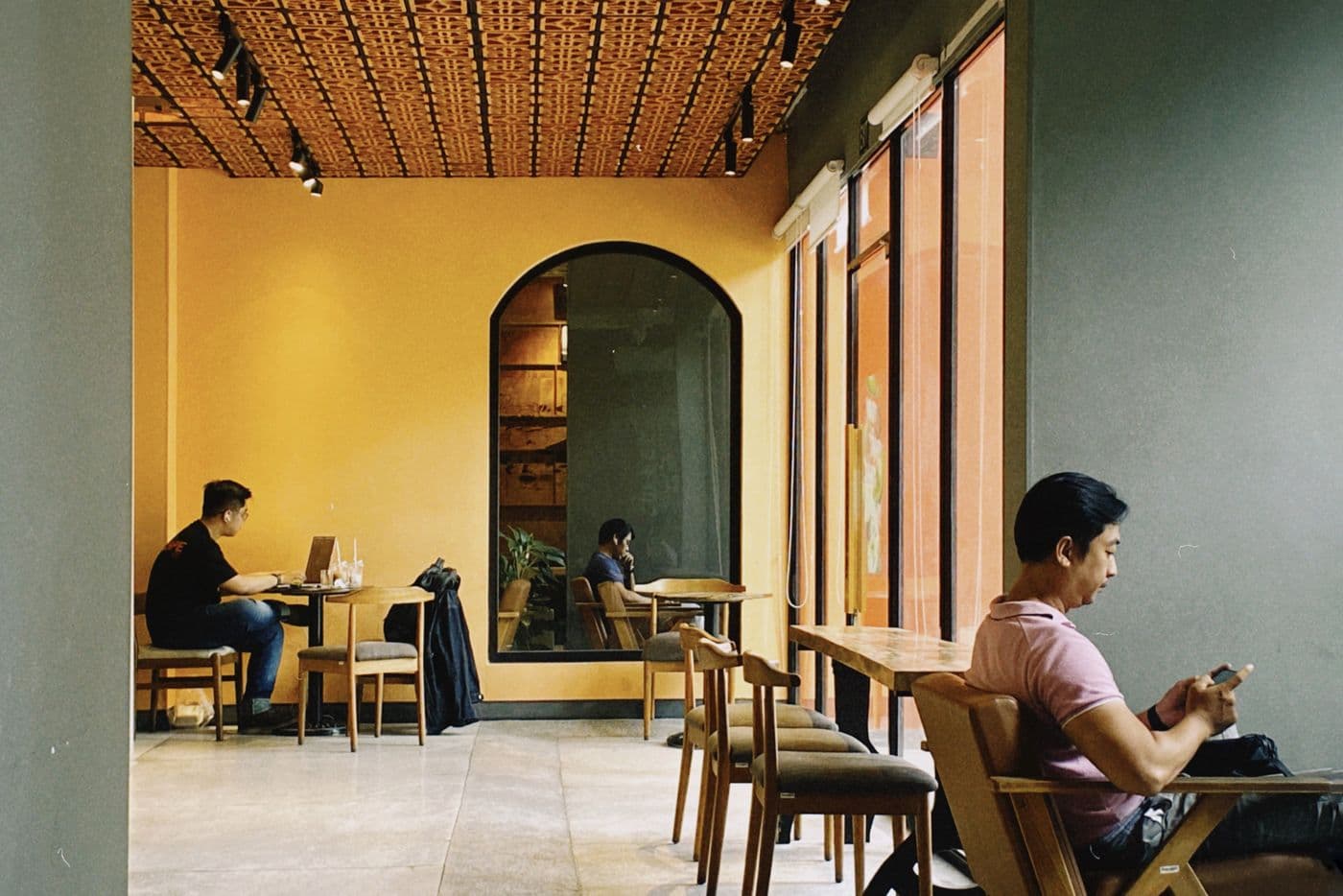 A Ho Chi Minh City coffee shop: one man works at a laptop by the window, another checks his phone