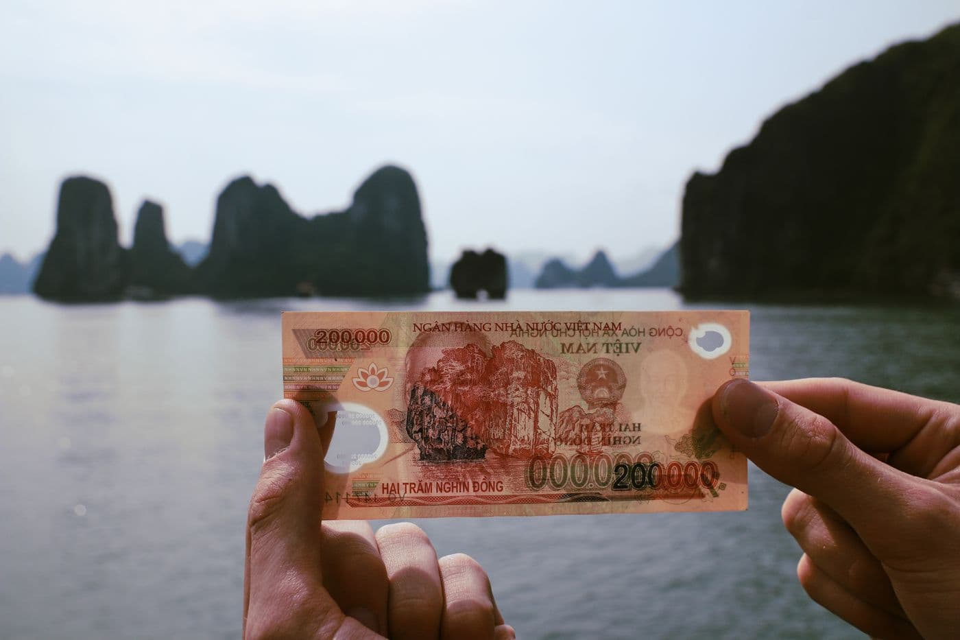 A 200,000-dong note held up against Ha Long Bay, the scene printed on that same banknote